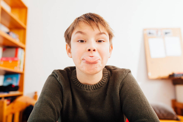 Ten year old school boy sticking out tongue in home video schooling situation, close up looking into wide angle camera - Фото, зображення