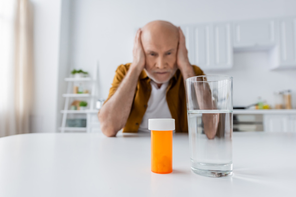 Pills and glass of water near blurred pensioner at home  - Foto, immagini
