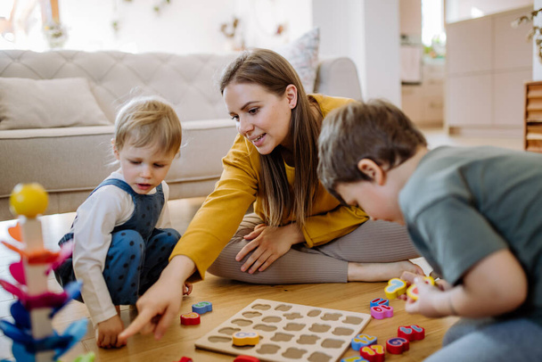 Young mother and kids playing with montessori wooden toys in living room, having nice family time together. - Фото, зображення