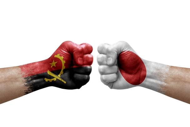 Two hands punch to each others on white background. Country flags painted fists, conflict crisis concept between angola and japan - Photo, Image