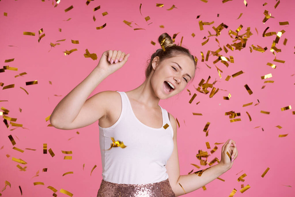 Caucasian teenage girl on pink background dancing among golden confetti  - Фото, зображення