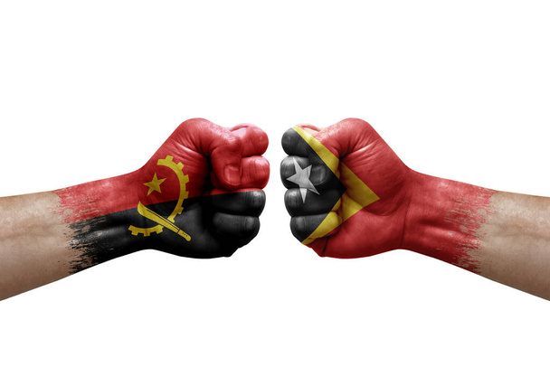 Two hands punch to each others on white background. Country flags painted fists, conflict crisis concept between angola and timor leste - Photo, Image