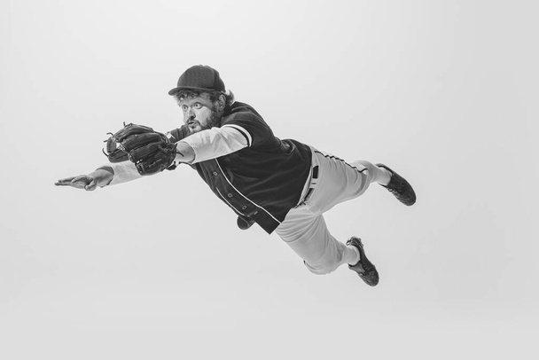 Flight. Monochrome portrait of male baseball player wearing retro sports uniform and holding bat isolated on white background. Vintage baseball batter in jump. Concept of sport, fashion, emotions, ad - Foto, imagen