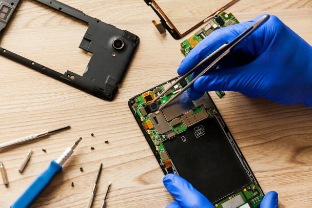 The technician repairing the smartphones motherboard in the workshop on the table. Concept of mobile phone, electronic, upgrade and technology. - Zdjęcie, obraz