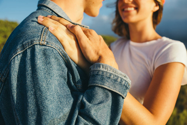 Midsection of romantic young boyfriend holding girlfriend's hand on his shoulder while enjoying sunset during weekend getaway - Fotografie, Obrázek