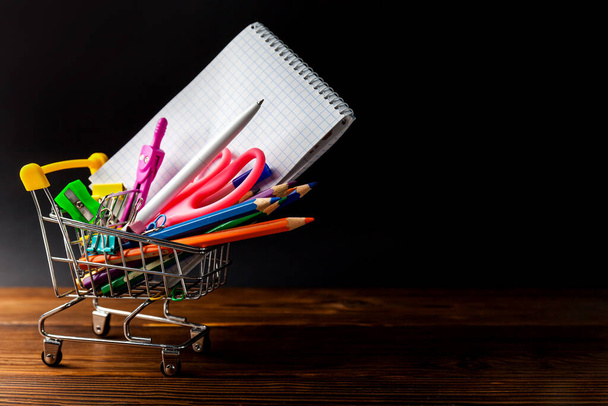 Shopping cart full of stationery or office supplies on dark background. Back to school concept. - Foto, Imagen