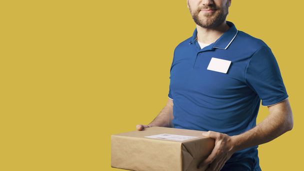 Smiling delivery man holding a box, delivery and shipment concept - Foto, imagen