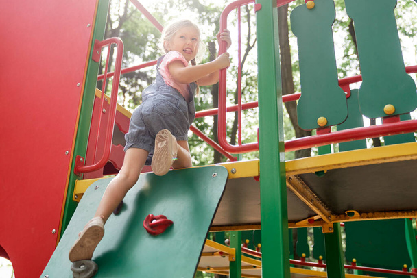 Smiling little girl climbing at the playground in summer day                                 - Фото, изображение