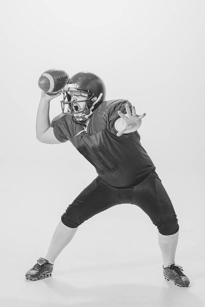 Shooting a ball. Black and white portrait of american football player in vintage style sports uniform isolated on white background. Concept of sport, eras comparison, timeless traditions, skills and - Фото, изображение