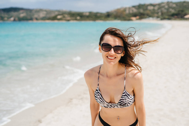 Portrait of a cheerful woman looking at the camera smiling in sunglasses on an island landscape holiday. The concept of vacation, tourism and carefree lifestyle in nature - Foto, Imagen