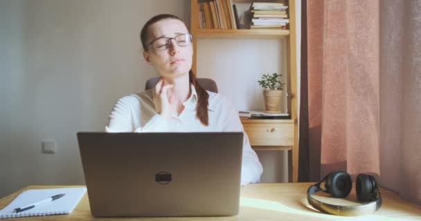 Young woman yawns while sitting workplace, laptop, desktop, looks out window. Front view, portrait. Concept of work fatigue, overwork, boring work, home office, learning, freelancing, student. High - Séquence, vidéo