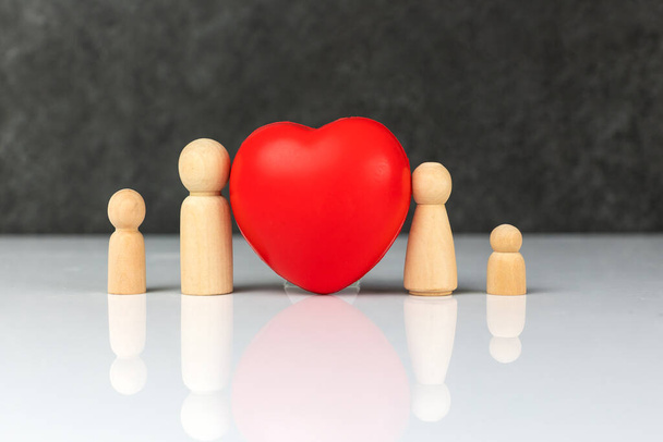 Four small wooden figurines that symbolize a family - a mother, a father and two children, near a big red heart. The concept of family love and care. Life insurance concept. - Photo, Image