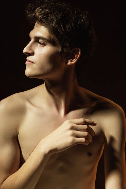 Ελληνικό προφίλ. Κοντινό πορτραίτο ενός νεαρού όμορφου άντρα χωρίς πουκάμισο, απομονωμένου σε σκούρο vintage φόντο. Φυσική ομορφιά. Τέχνη, νεολαία, μόδα, ρετρό στυλ, ad concept. - Φωτογραφία, εικόνα