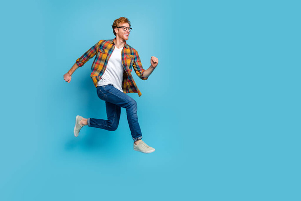 Photo of funky handsome cheerful guy wear checkered shirt with red hairstyle running flying rush isolated on blue color background. - Photo, Image