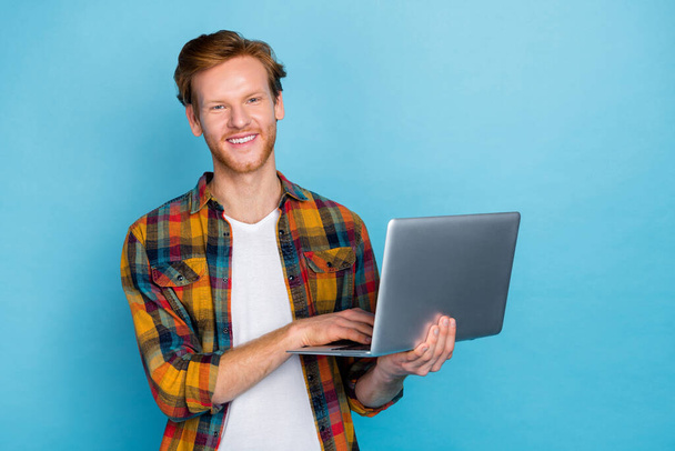 Photo of clever handsome cheerful guy with ginger hair dressed plaid shirt typing code at remote job isolated on blue color background. - Foto, Imagem