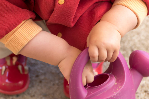 close up of a baby's hands playing with a watering can, outside activity, fine motor skills development - Foto, immagini