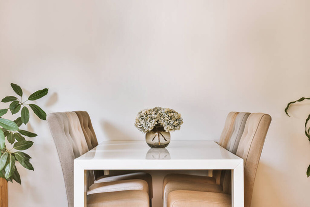 Moderno design degli interni in stile minimalista di monolocale con cucina bianca aperta e zona pranzo con tavolo e sedie illuminati da lampada in stile loft - Foto, immagini