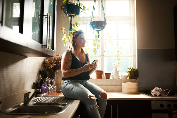 Как я должен на это реагировать? молодая женщина пользуется смартфоном на кухне дома - Фото, изображение