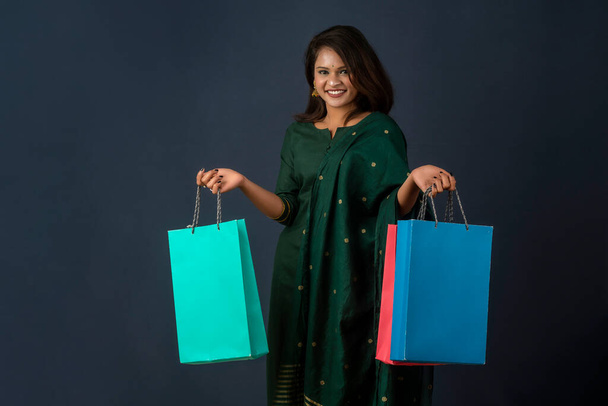 Beautiful Indian young girl or woman holding and posing with shopping bags on a dark background - Foto, afbeelding