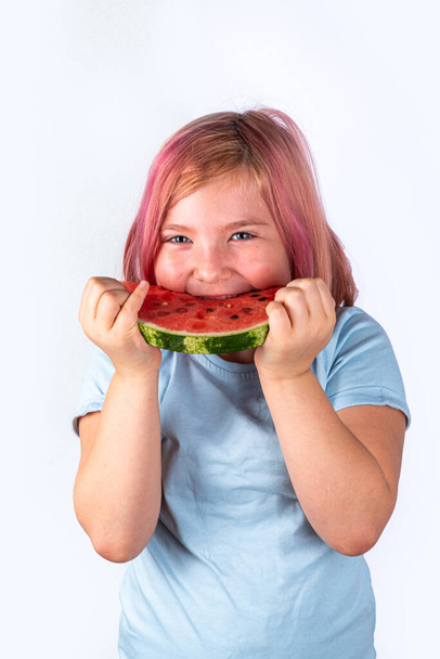 Concept of enjoying summer, light autumn harvest, vacation holiday. Cute attractive european blonde child girl eating a big piece of juicy sweet red watermelon - Foto, Bild