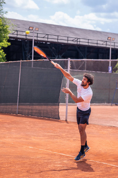 Концентроване спортивне обладнання чоловік тенісист тренування для чемпіонату він грає на відкритому повітрі тенісна гра на глиняному дворі в сонячний літній день
. - Фото, зображення