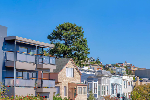 Houses with different exterior in San Francisco, California. There is a house on the left with glass on its balconies beside the house with stone walls along with the other houses with wood sidings. - Foto, immagini