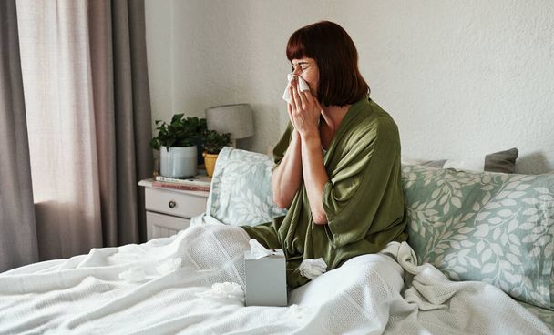Im as sick as a puppy today. an attractive young woman feeling sick and blowing her nose with a tissue inside her bedroom at home - Fotografie, Obrázek