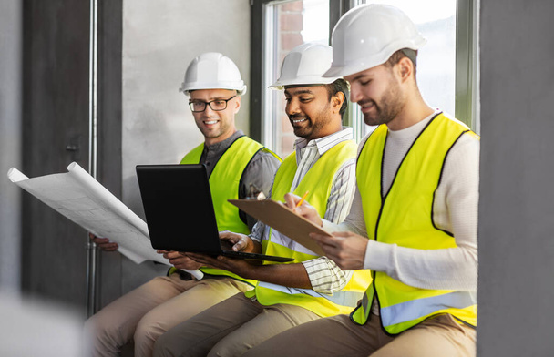 architecture, construction business and people concept - group of male architects in helmets with laptop, blueprint and clipboard working at office - Фото, зображення