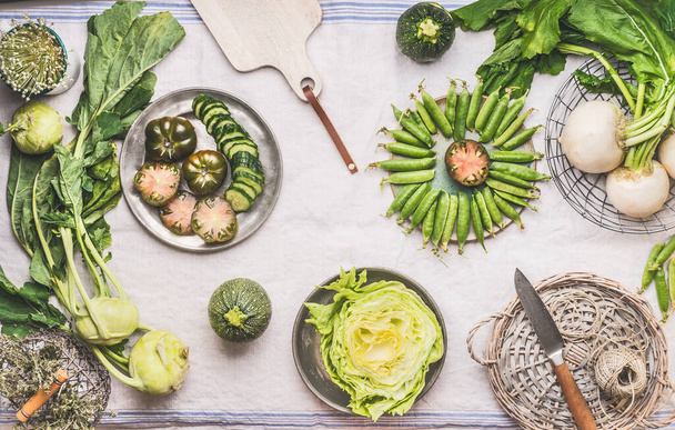 Flat lay green vegetables in bowls on light table with knife: green peas, kohlrabi, lettuce, zucchini, cucumber, green tomatoes. Top view. Clean vegetarian eating and cooking concept. - Foto, afbeelding