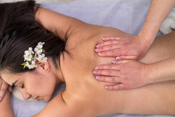 Крупным планом женских рук выполняется терапевтический массаж для женщины-клиента, отдыхающей на столе в спа-салоне. Концепция ухода за телом - Фото, изображение