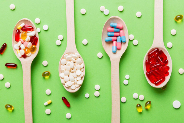 Vitamin capsules in a spoon on a colored background. Pills served as a healthy meal. Red soft gel vitamin supplement capsules on spoon. - Foto, Imagem