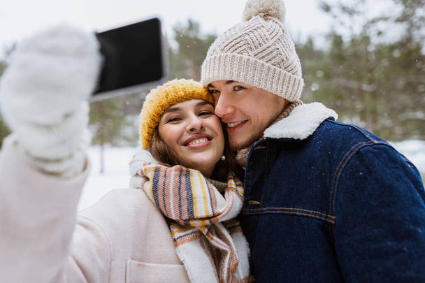 season, technology and leisure concept - happy couple with smartphone taking selfie in winter park - Valokuva, kuva