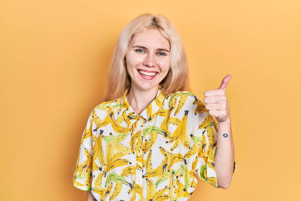 Piękna biała kobieta z blond włosami w kolorowe koszulki uśmiechnięta szczęśliwy i pozytywny, kciuk w górę robi doskonałe i znak aprobaty  - Zdjęcie, obraz