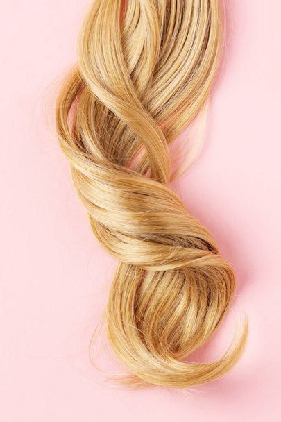 Long golden blond curly hair. A part of blond hair top view on pink background. - Foto, immagini