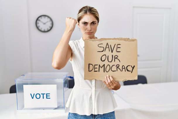 Mladá blondýnka v politických volbách zachraňuje transparent demokracie, rozzlobená a frustrovaná, křičící vzteky a zvednutou rukou  - Fotografie, Obrázek