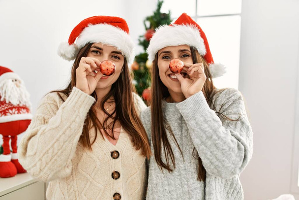 Twee vrouwen glimlachen zelfverzekerd met kerstbal op de neus thuis - Foto, afbeelding