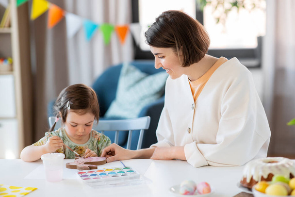 holidays, family and people concept - happy mother and little baby daughter coloring easter bunny with watercolors at home - Fotografie, Obrázek