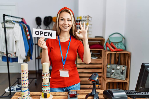 Young caucasian woman holding banner with open text at retail shop doing ok sign with fingers, smiling friendly gesturing excellent symbol  - Zdjęcie, obraz