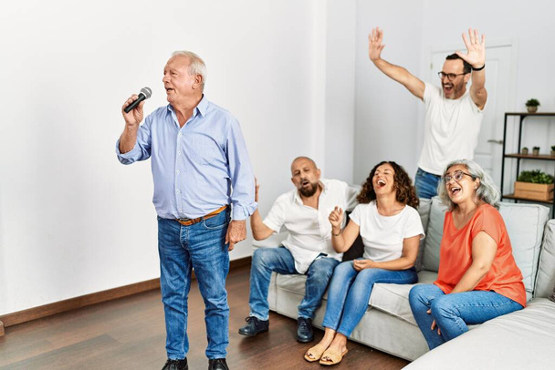 Groep van middelbare leeftijd vrienden die feestgezang zingen met behulp van microfoon thuis. - Foto, afbeelding
