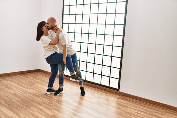 Молодая латиноамериканская пара улыбается счастливо танцуя в пустом новом доме. - Фото, изображение
