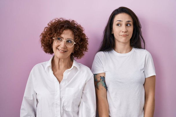 Hispanic mother and daughter wearing casual white t shirt over pink background smiling looking to the side and staring away thinking.  - Photo, Image