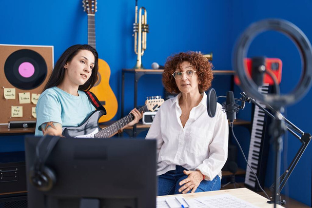 Two women musicians having online electrical guitar lesson by smartphone at music studio - Foto, Imagem