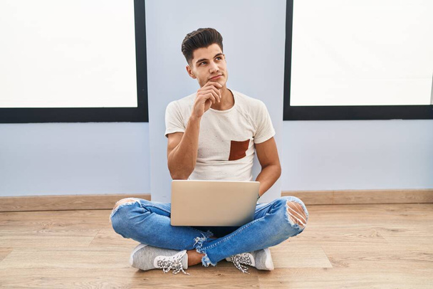 Young hispanic man using laptop at home with hand on chin thinking about question, pensive expression. smiling with thoughtful face. doubt concept.  - Foto, immagini
