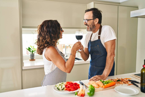 Spanisches Paar mittleren Alters kocht und prostet mit Wein in der Küche zu - Foto, Bild
