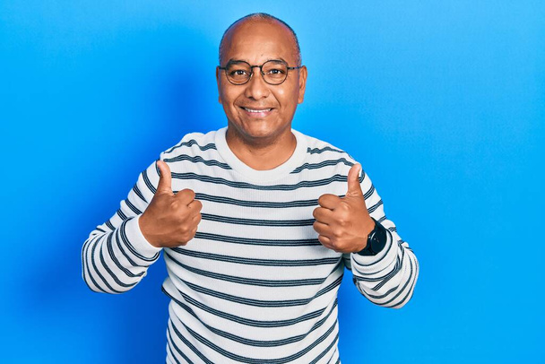 Middle age latin man wearing casual clothes and glasses success sign doing positive gesture with hand, thumbs up smiling and happy. cheerful expression and winner gesture.  - Photo, Image