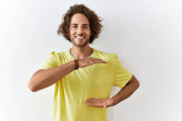 Jeune homme hispanique debout sur fond isolé gestuelle avec les mains montrant grand et grand signe de taille, symbole de mesure. souriant en regardant la caméra. concept de mesure.  - Photo, image