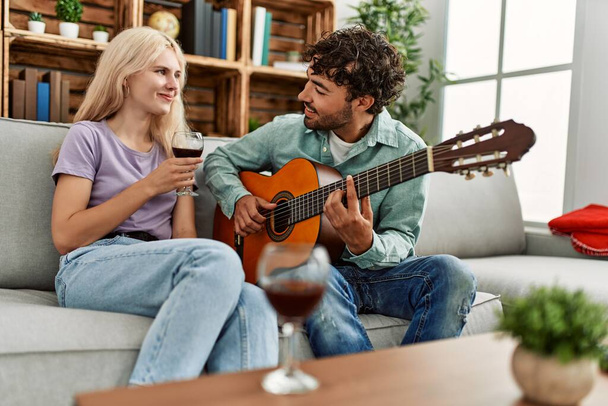 Mężczyzna gra na hiszpańskiej gitarze do swojej dziewczyny siedzi na kanapie w domu. - Zdjęcie, obraz
