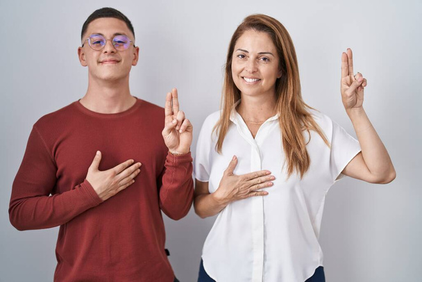Mother and son standing together over isolated background smiling swearing with hand on chest and fingers up, making a loyalty promise oath  - Foto, Imagem