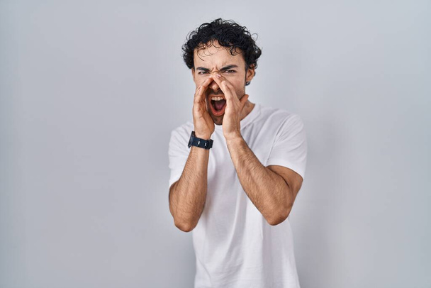Латиноамериканец, стоящий на изолированном заднем плане, громко кричащий сердито с руками над ртом  - Фото, изображение