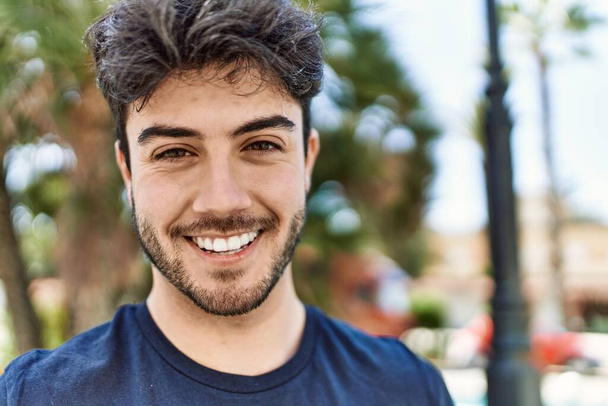 Молодой латиноамериканец улыбается счастливо стоя в городе. - Фото, изображение